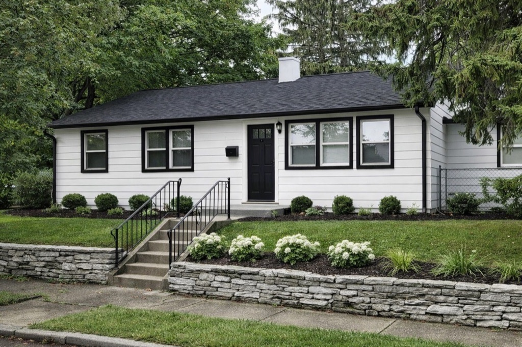 1919 Kendall Street after renovation: white lap siding, black trim and door, new plantings above a stone retaining wall.