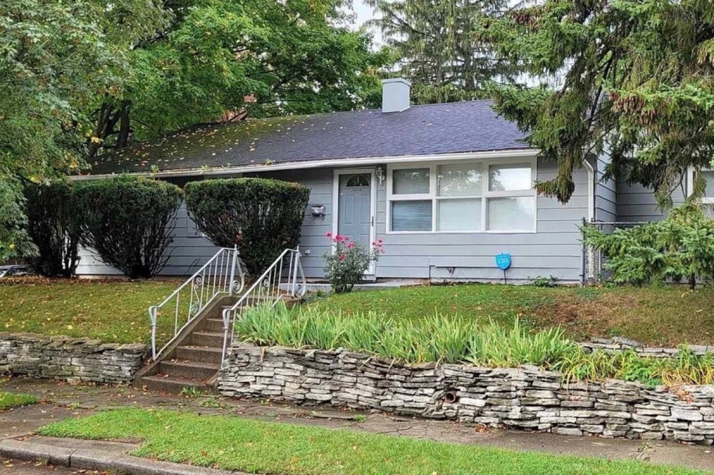 1919 Kendall Street before renovation: grey siding, overgrown shrubs, weathered railing.