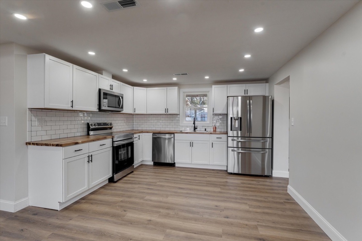 Kitchen after renovation: white shaker cabinets, butcher block counters, subway tile, stainless appliances.