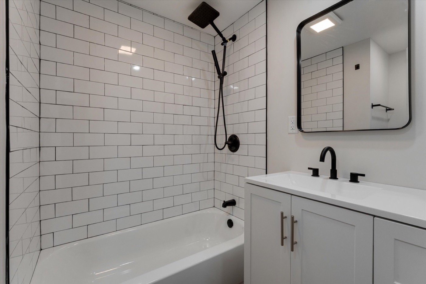 Bathroom after renovation: white subway tile bath surround, black fixtures, new vanity and mirror.