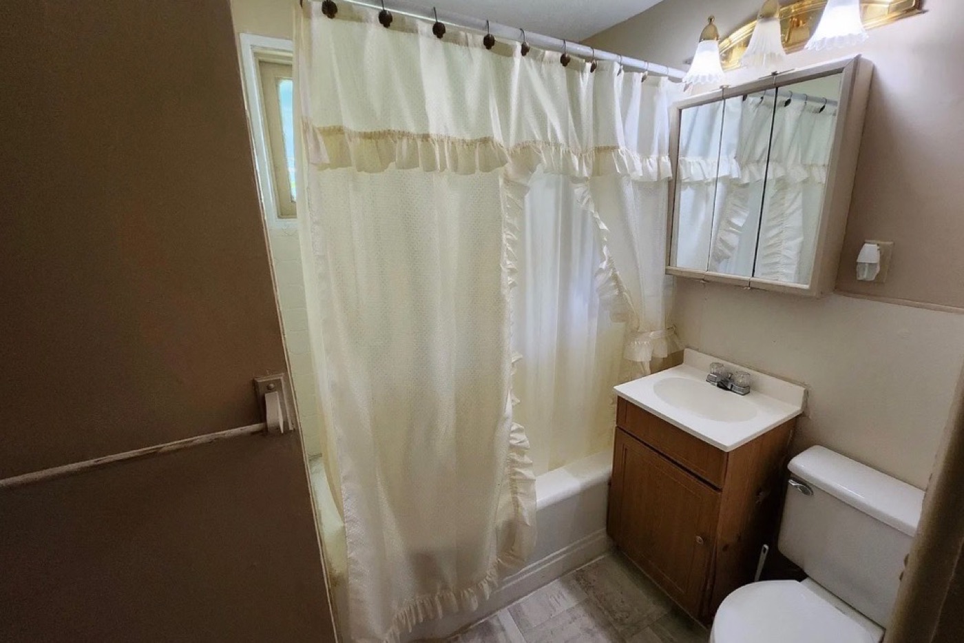 Bathroom before renovation: curtained tub, dated wood vanity, surface-mounted medicine cabinet.