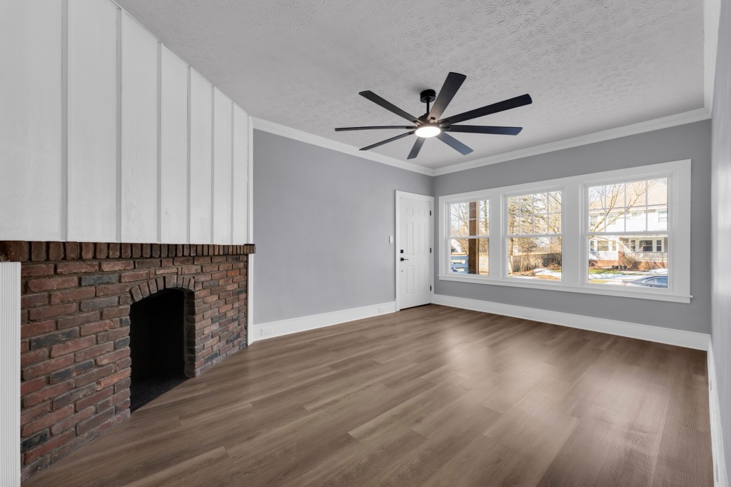 Living room at 3220 Clarendon Road after renovation: brick fireplace, board-and-batten chimney breast, three front windows.