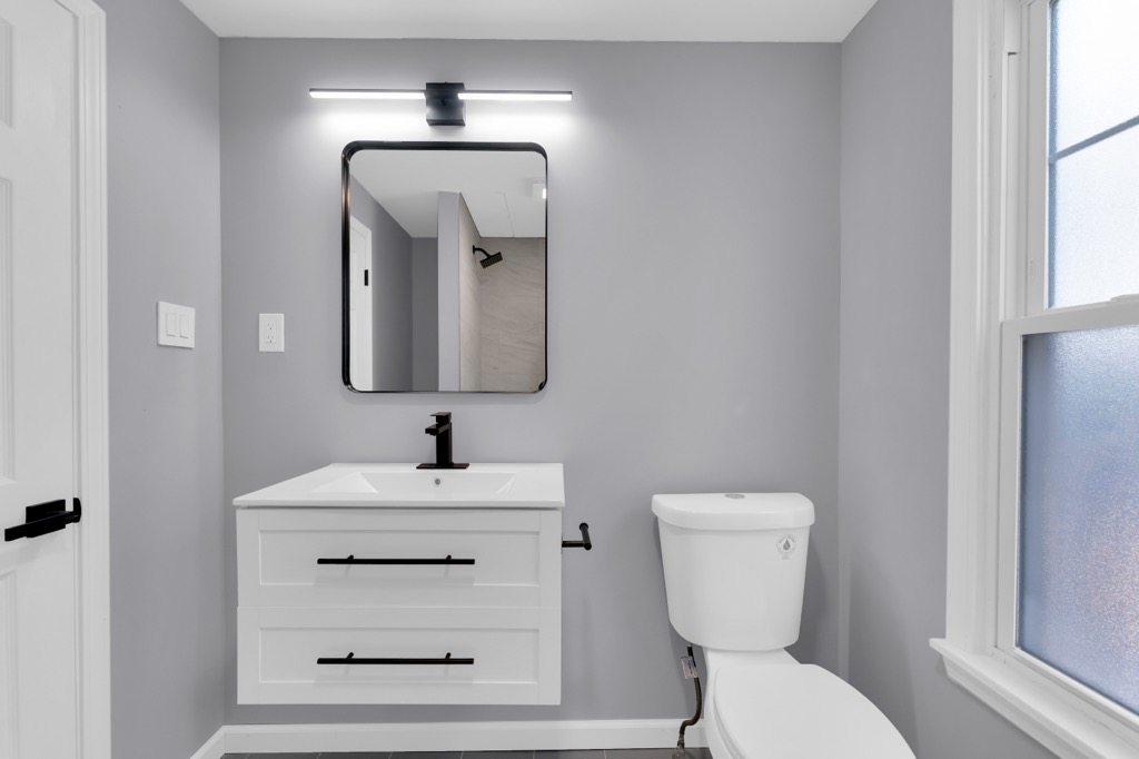 Bathroom after renovation: floating vanity, black-framed mirror and fixtures, frosted window.