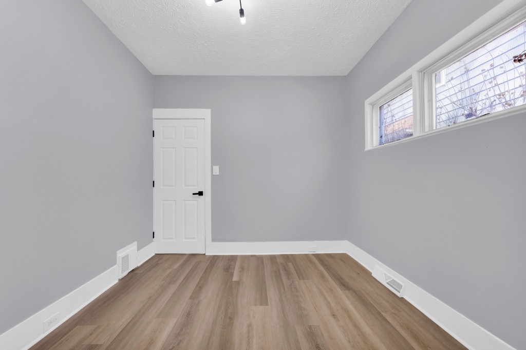 Bedroom after renovation: grey walls, new plank flooring, high windows.