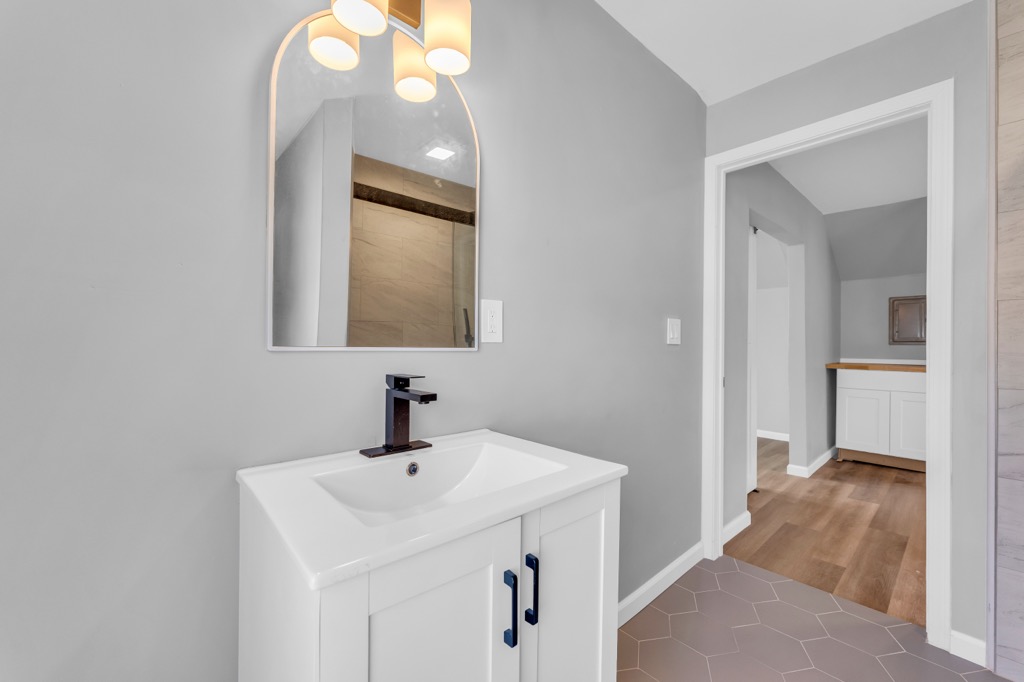 Upstairs bathroom vanity after renovation with arched mirror and black fixtures.