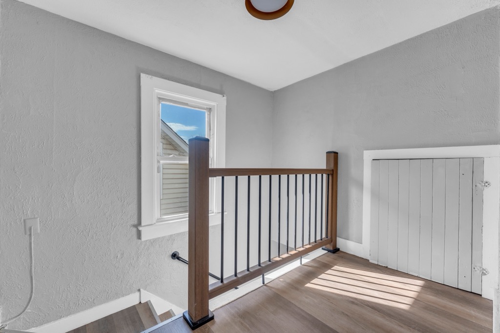 Stair landing in the upstairs unit after renovation: new railing, plank flooring, window.