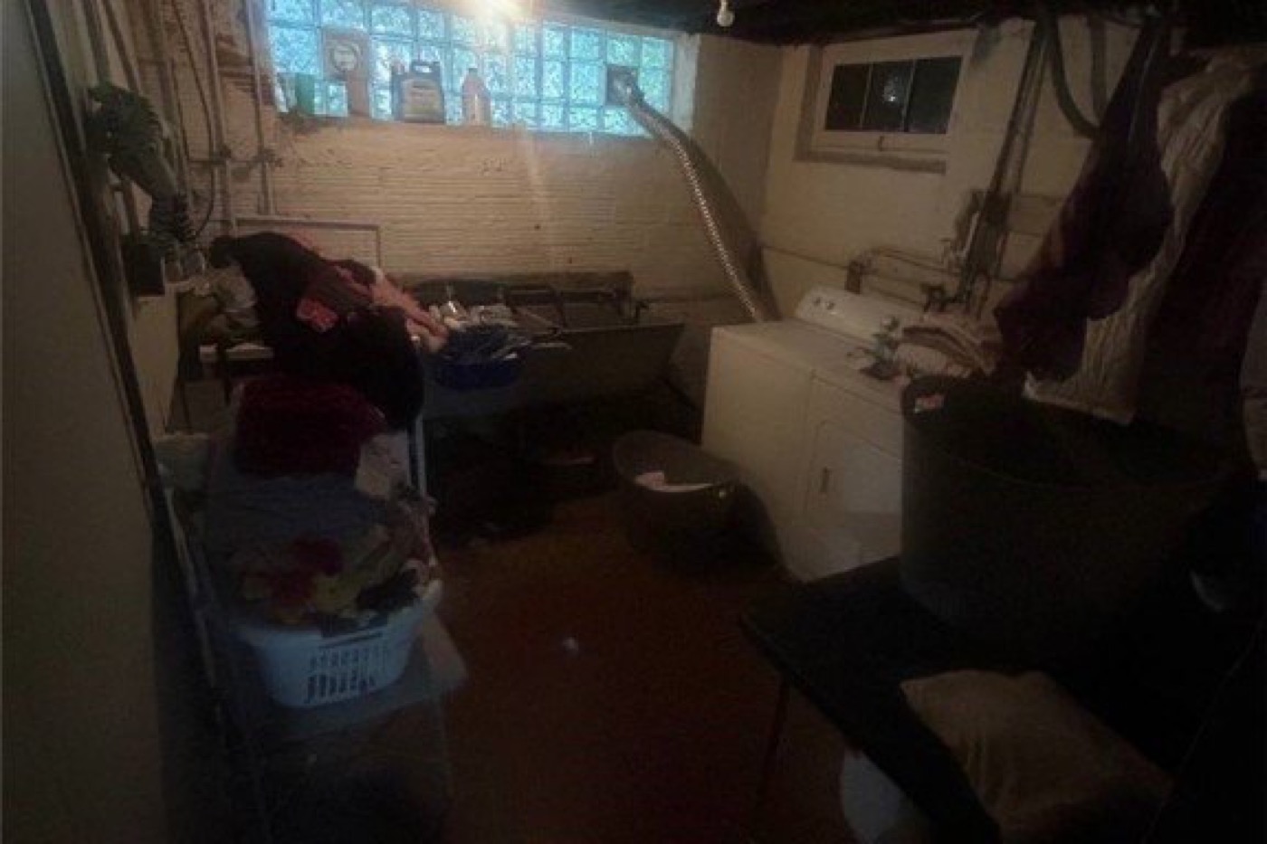 Basement laundry before renovation: dark unfinished room, glass-block window, old washer and utility sink.