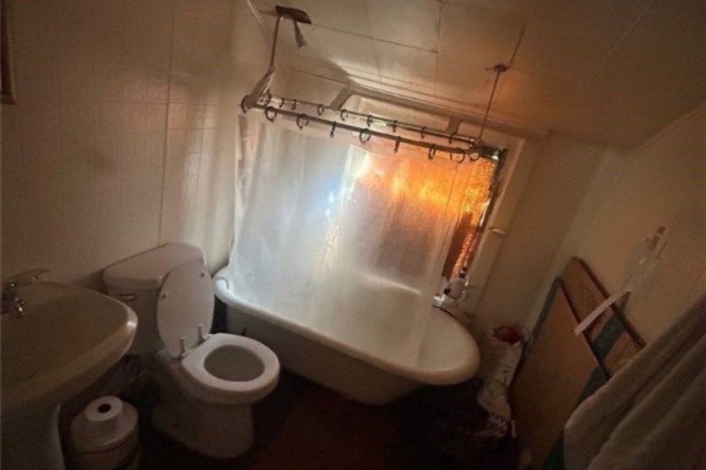 Upstairs bathroom before renovation: curtained tub under the sloped ceiling, toilet and pedestal sink on the left, dated tile.