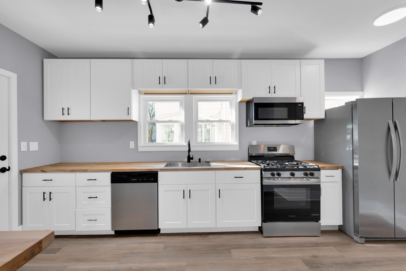 Kitchen after renovation: white shaker cabinets, butcher block counters, stainless range, dishwasher and refrigerator, window over the sink.