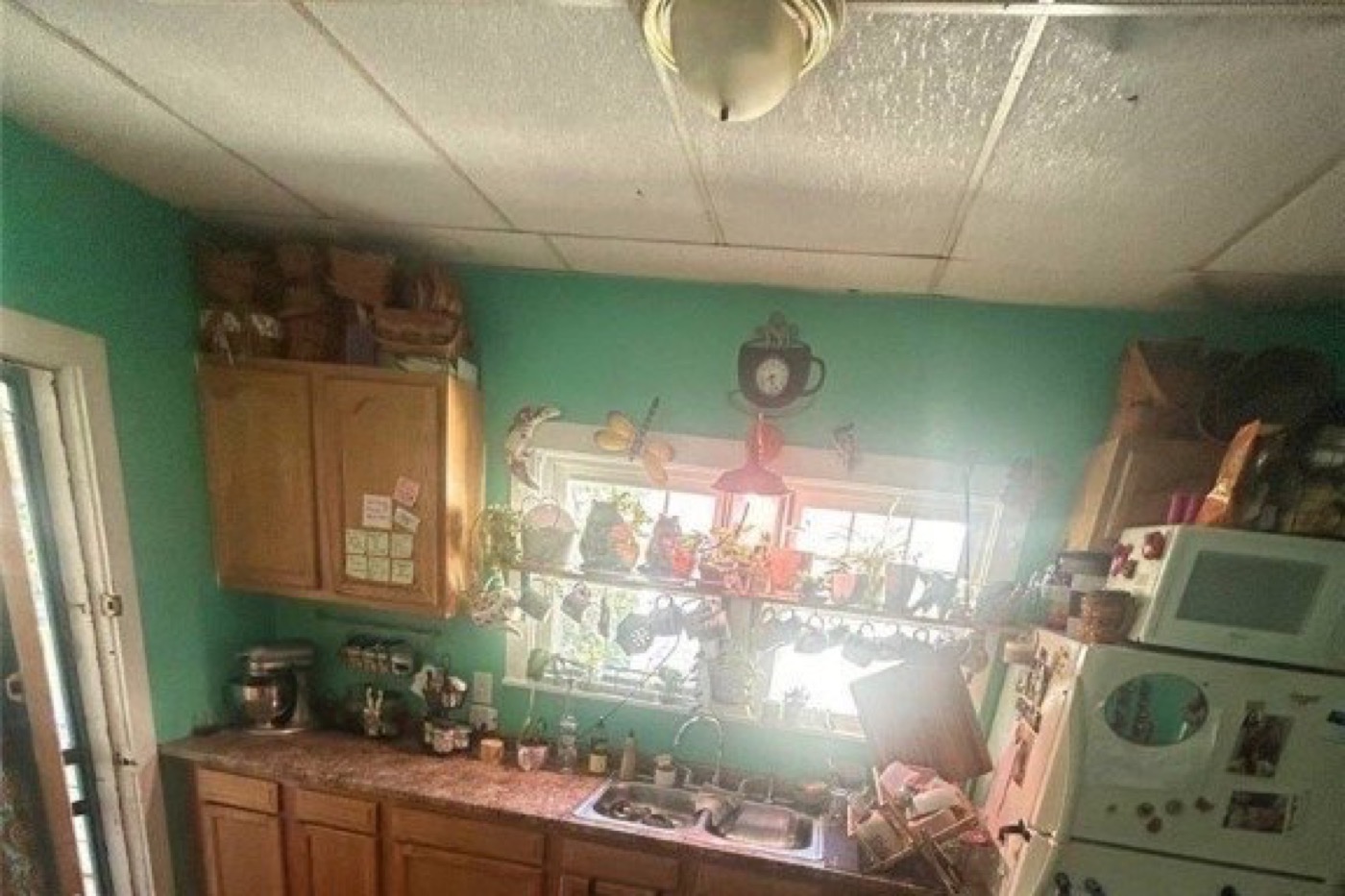 Kitchen before renovation: drop ceiling, wood cabinets, green walls, crowded counter under the window.