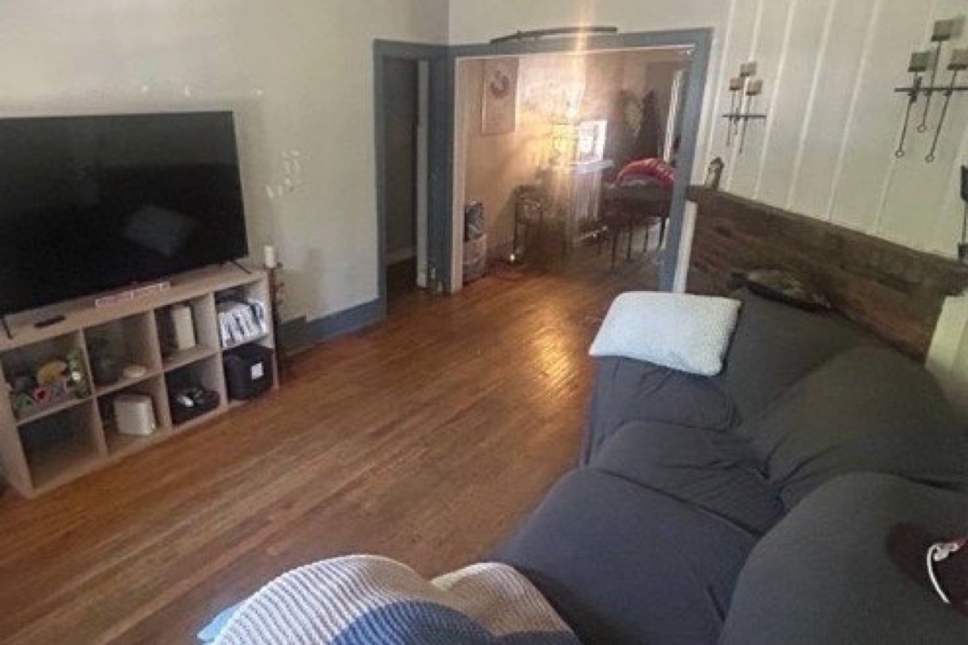 Living room before renovation: worn wood floor, sofa against the fireplace wall, dated trim, opening through to the next room.