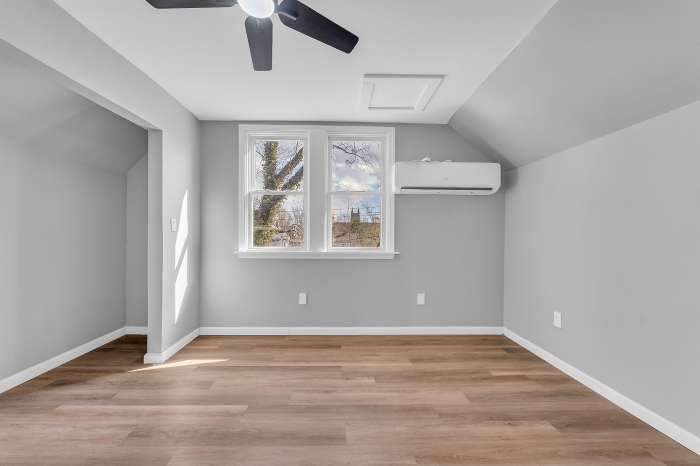 Upstairs living area after renovation: double window under the sloped ceiling, ductless mini-split, ceiling fan, new plank flooring.