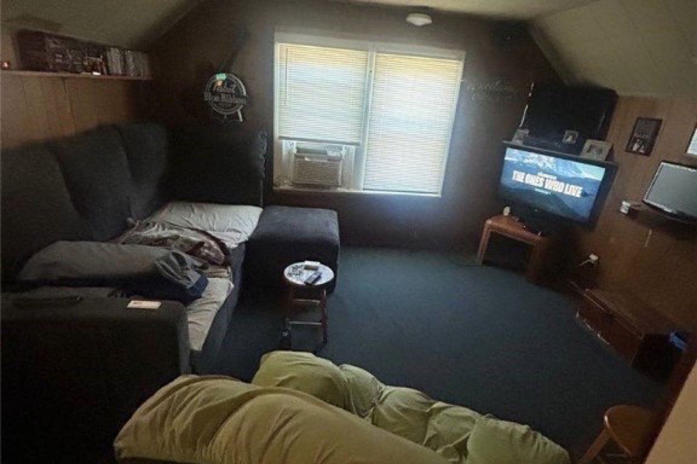 Upstairs living area before renovation: wood panelling, dark carpet, window air conditioner, sectional sofa.