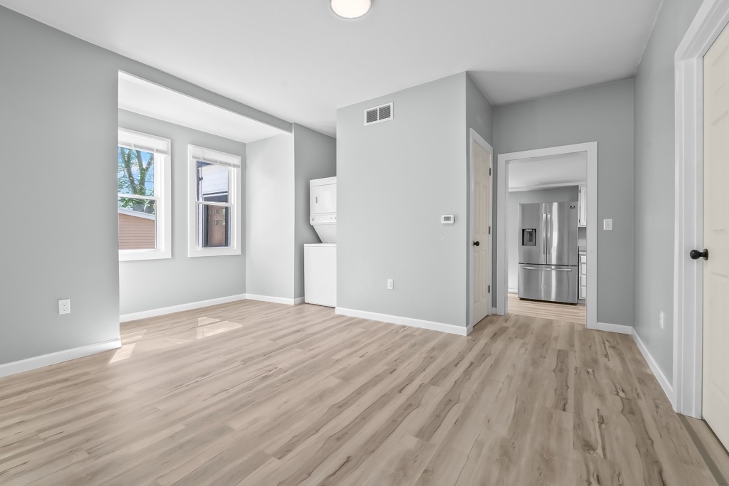 Open living space after renovation, looking toward the stacked laundry and stainless refrigerator.
