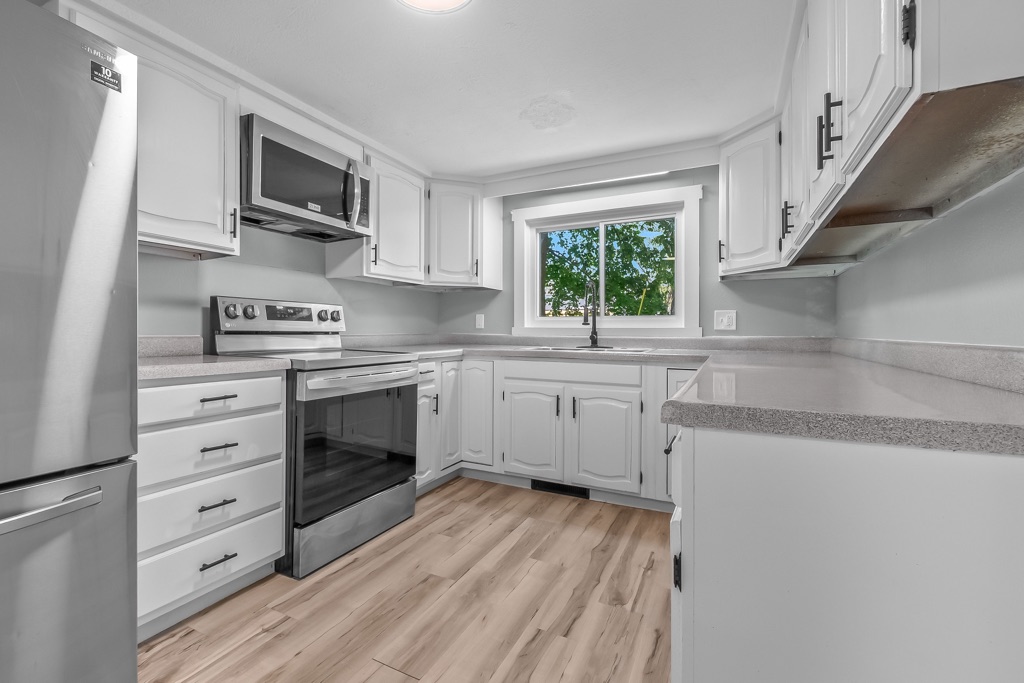 Kitchen after renovation: white cabinets, stainless range and microwave, window over the sink.