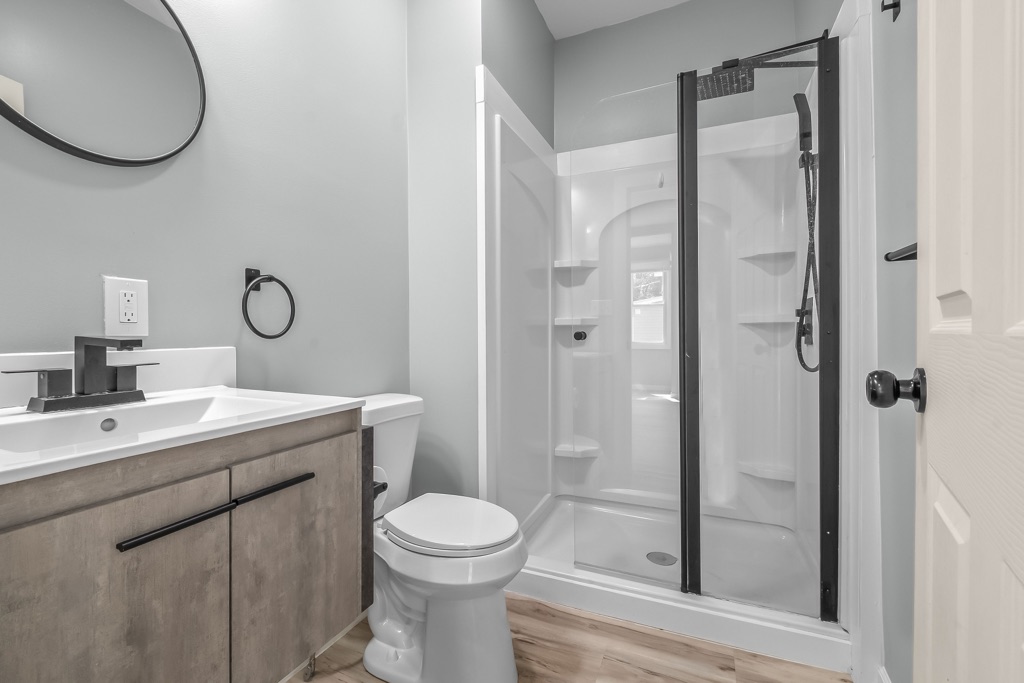 Bathroom after renovation: round mirror, walk-in shower with black frame, new vanity and toilet.