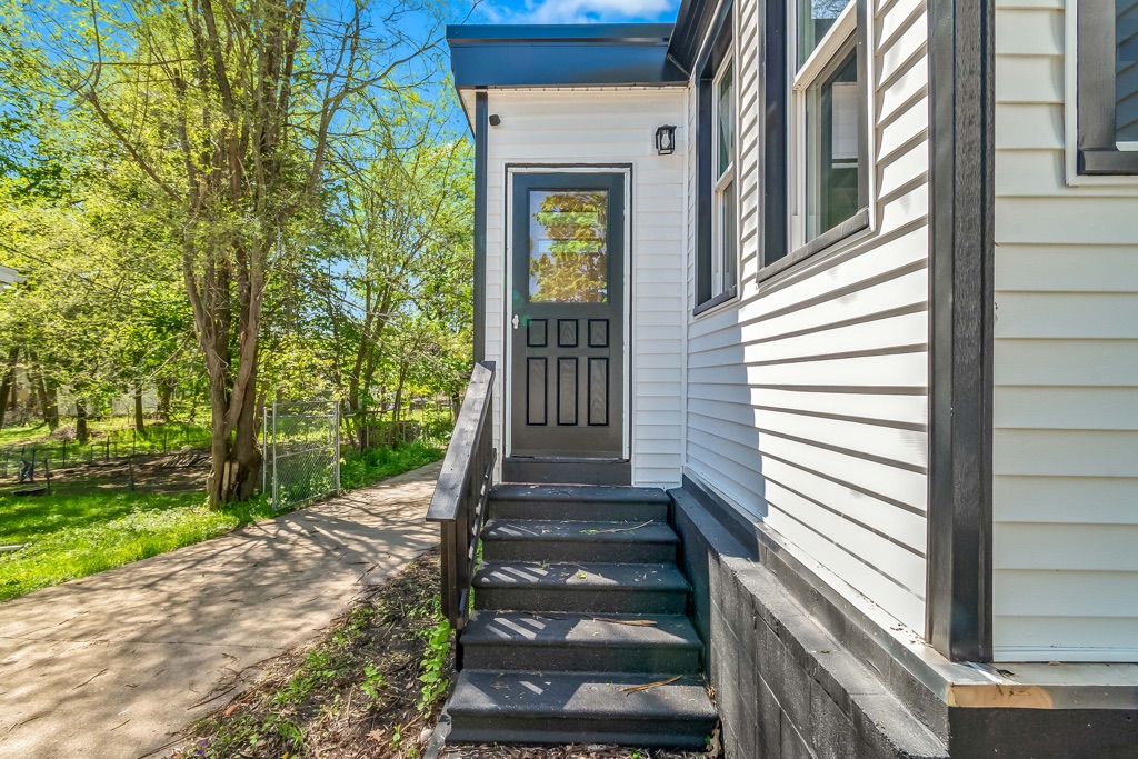 Side entry after renovation: new black door and steps against white lap siding.