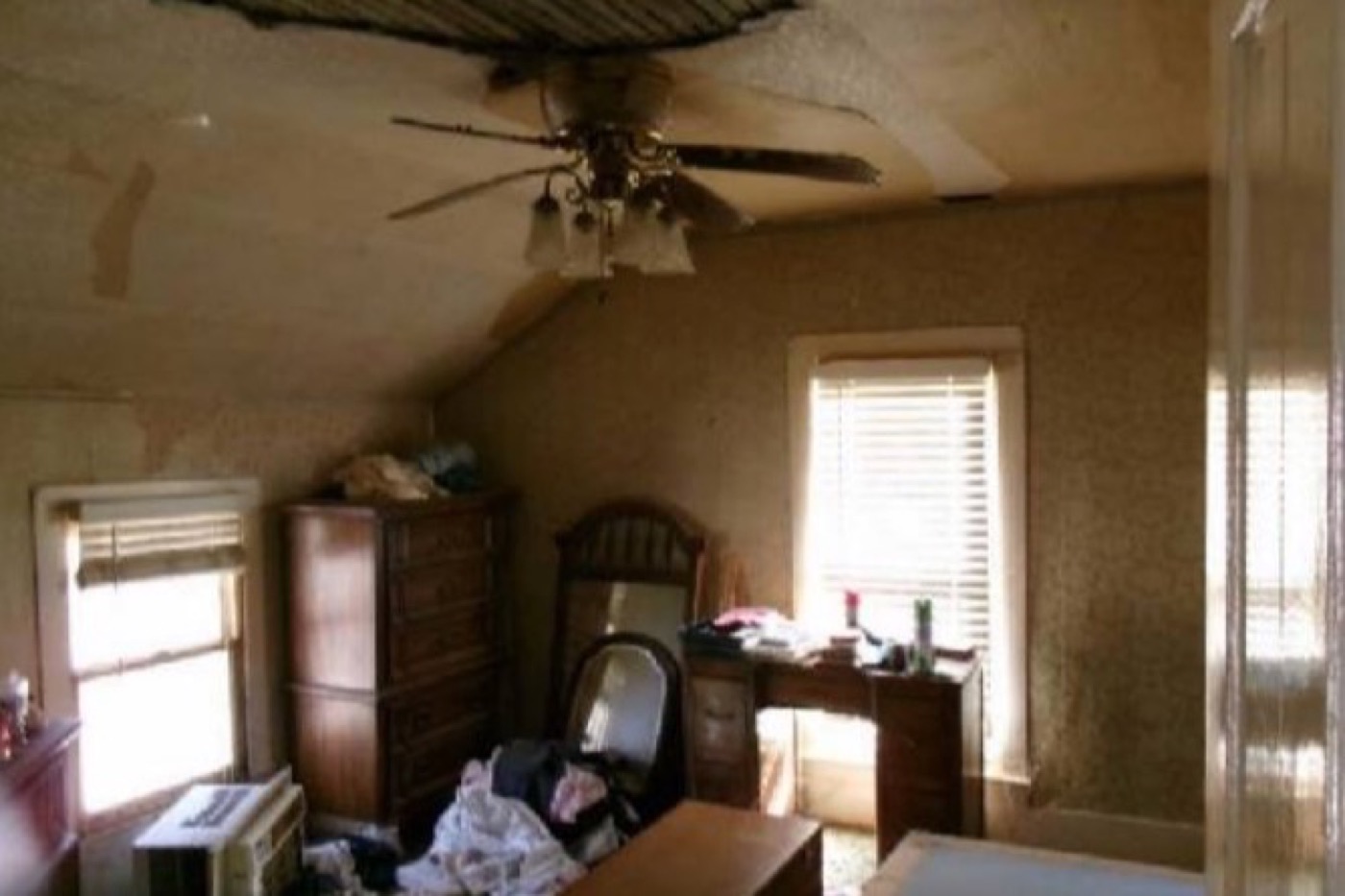 Bedroom before renovation: water-stained sagging ceiling, dated furniture and clutter, a window air conditioner.