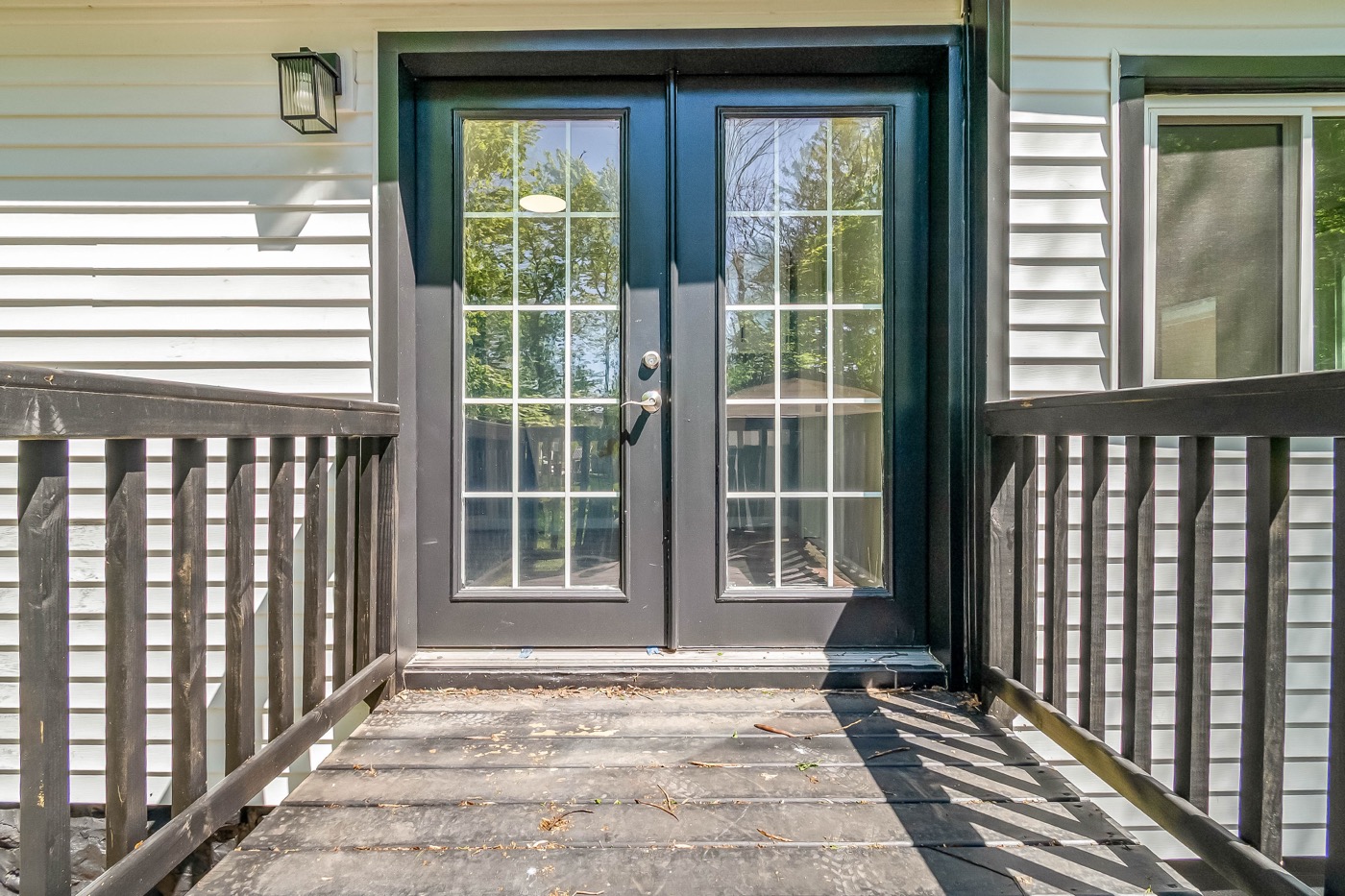 Rear deck after renovation: glass french doors with black frames opening onto a deck with dark railings and an exterior light.