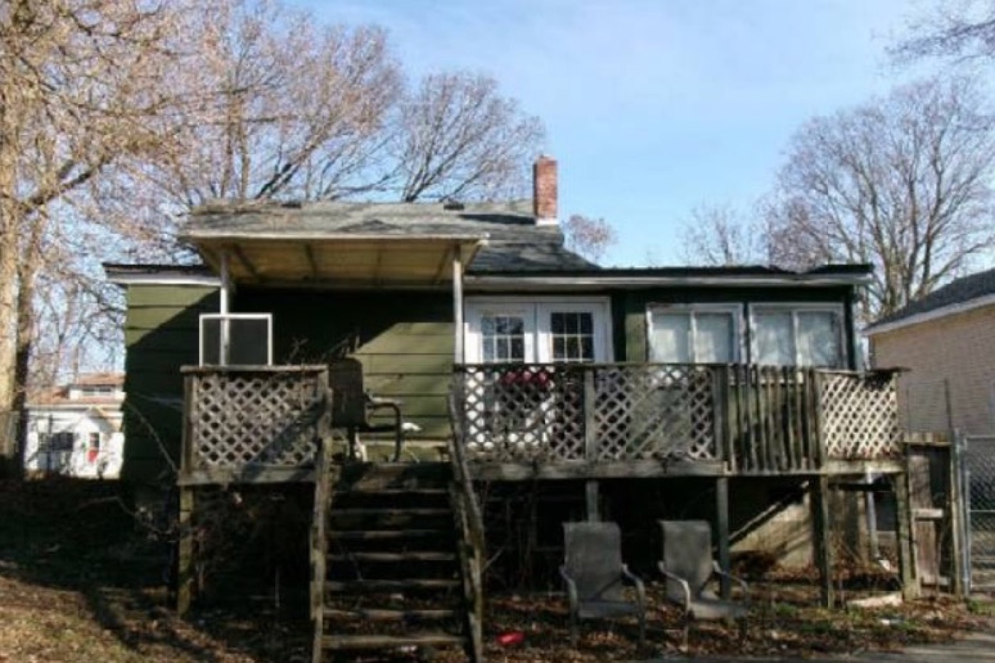 Rear of the house before renovation: aging covered deck with broken lattice skirting, weathered green siding, debris in the yard.
