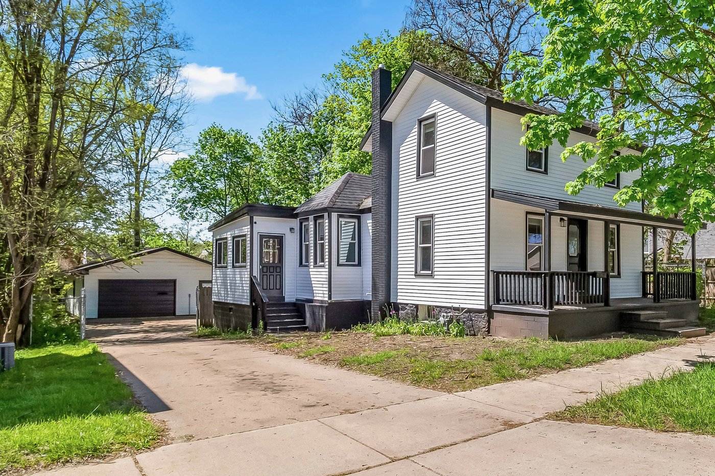 34 Mead Street after renovation: white lap siding with black trim, rebuilt front porch with black railings, brick chimney, tidy lawn and driveway.