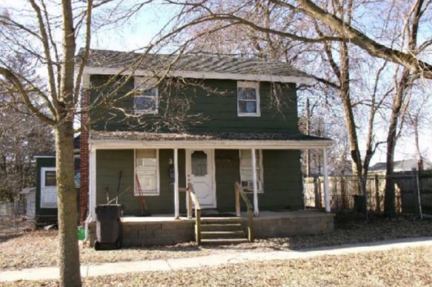34 Mead Street before renovation: dark weathered siding, a sagging full-width porch, bare dirt yard and overgrown fence line.