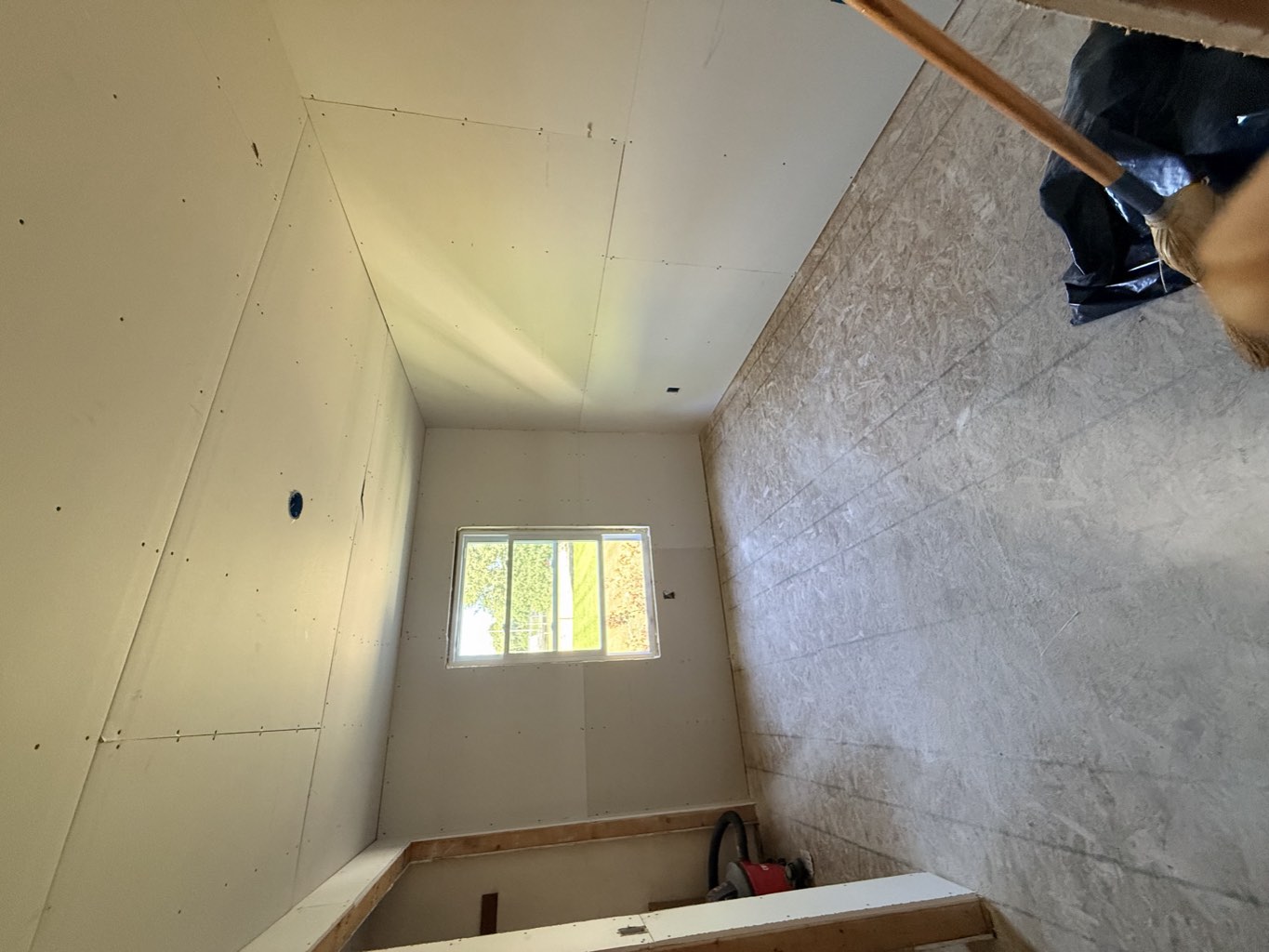 Bedroom with new drywall on the walls and ceiling and a window over the front lawn.