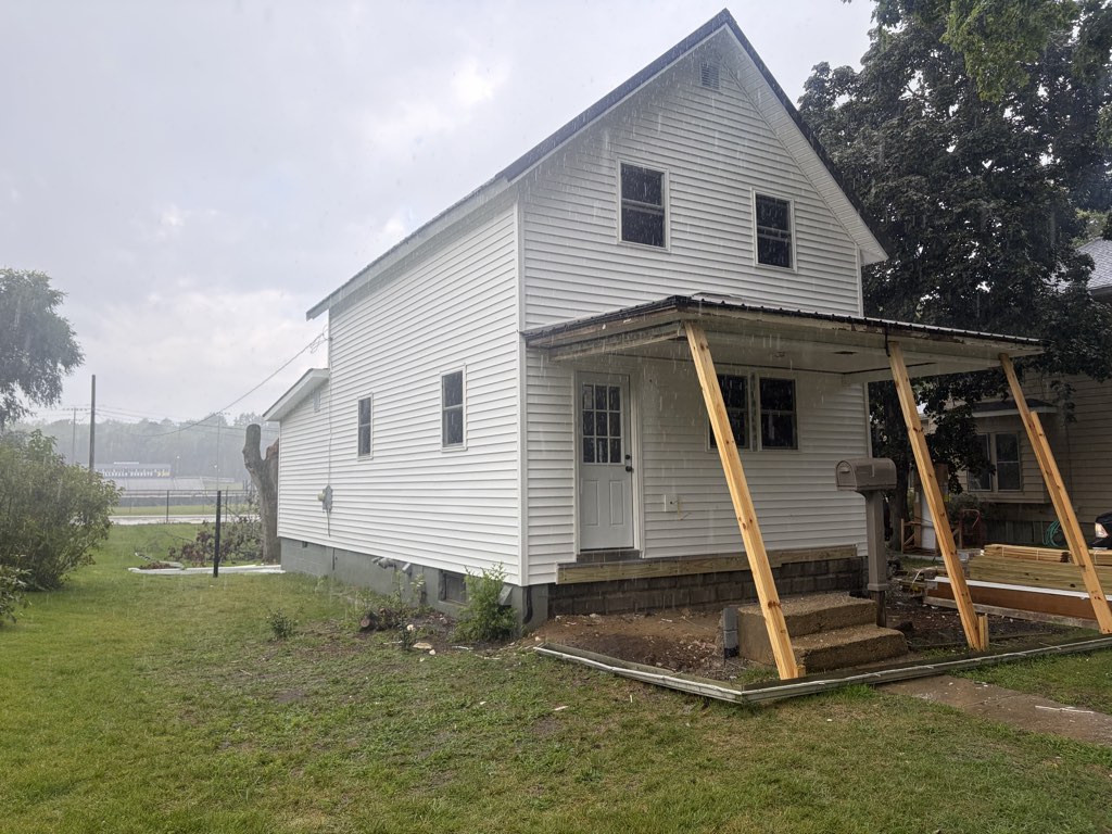 60 S Norwood Avenue mid-renovation: new white lap siding, new windows, front door under a porch roof on temporary bracing, standing-seam metal roof.