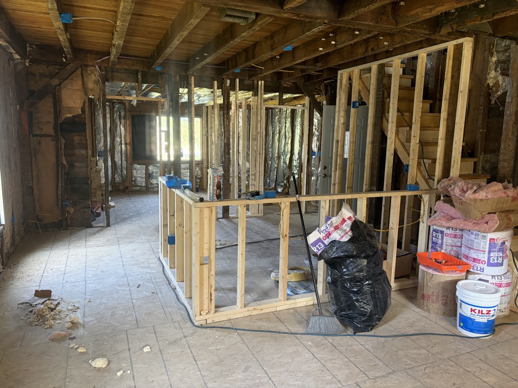 New stud framing standing on the main level in July, insulation and materials staged around the room.