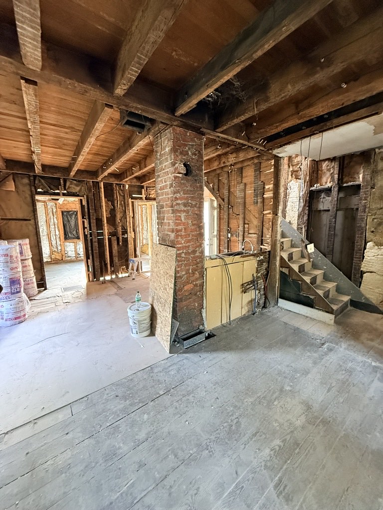 Gutted main level during demolition: exposed brick chimney, original staircase, bare stud walls and subfloor.