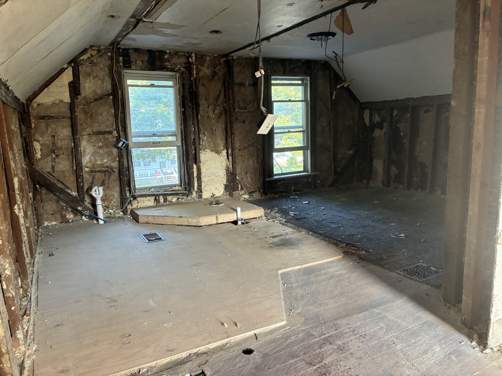 Upstairs gutted to the studs and subfloor under the sloped roofline, two windows over the street.