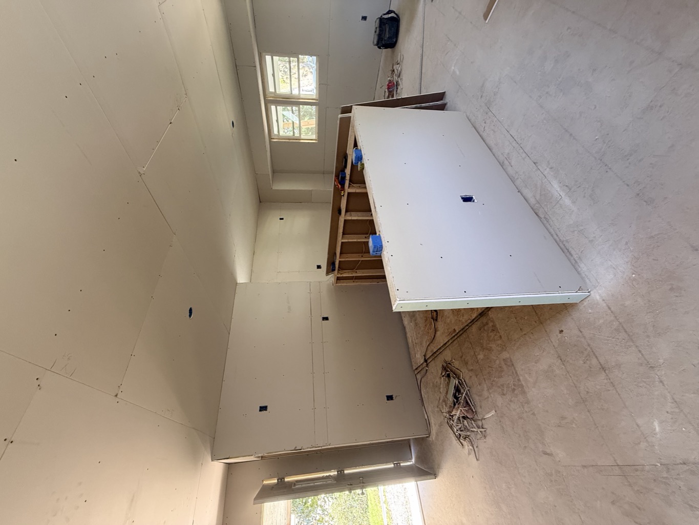 Open main living space with fresh drywall on the walls and ceiling, front door open to the yard.