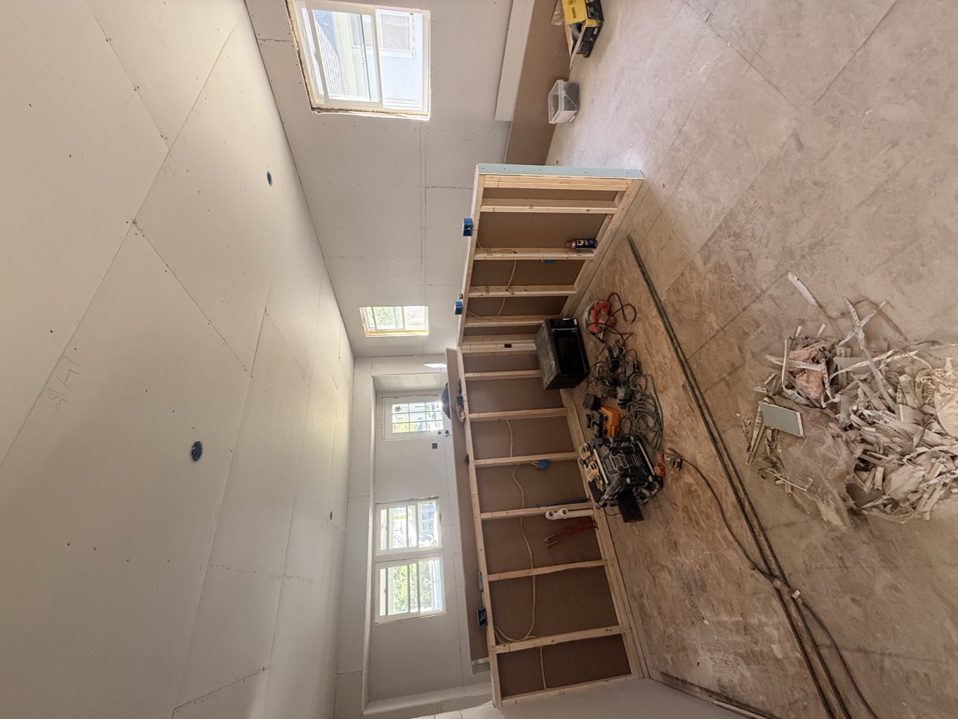 Main level with boarded ceilings and stud framing in place, tools staged on the subfloor.