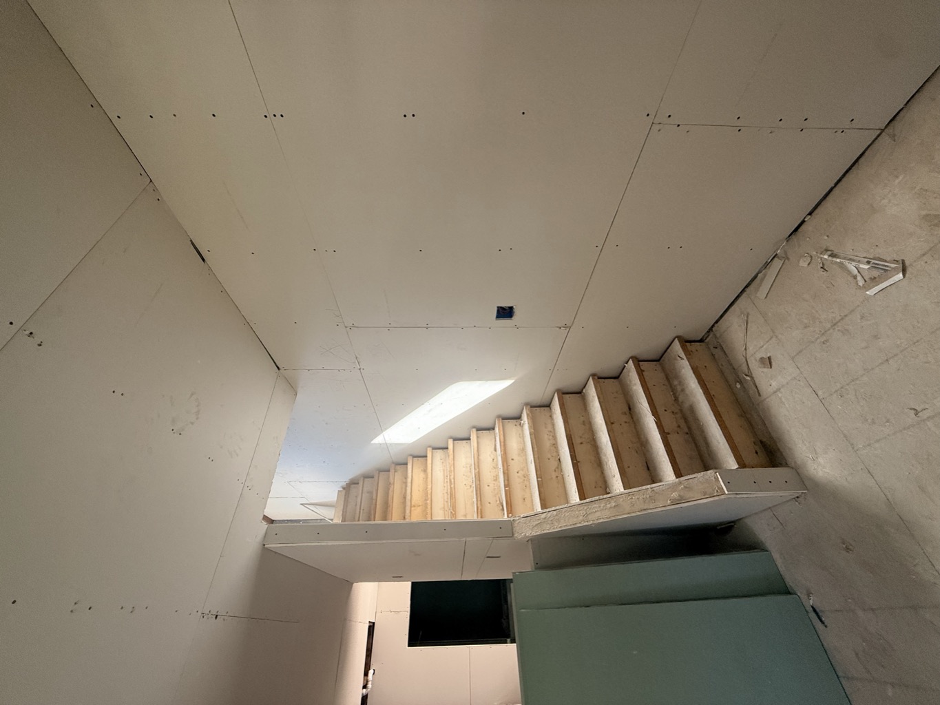 Staircase with new drywall along the stairwell and green board stacked at the base.