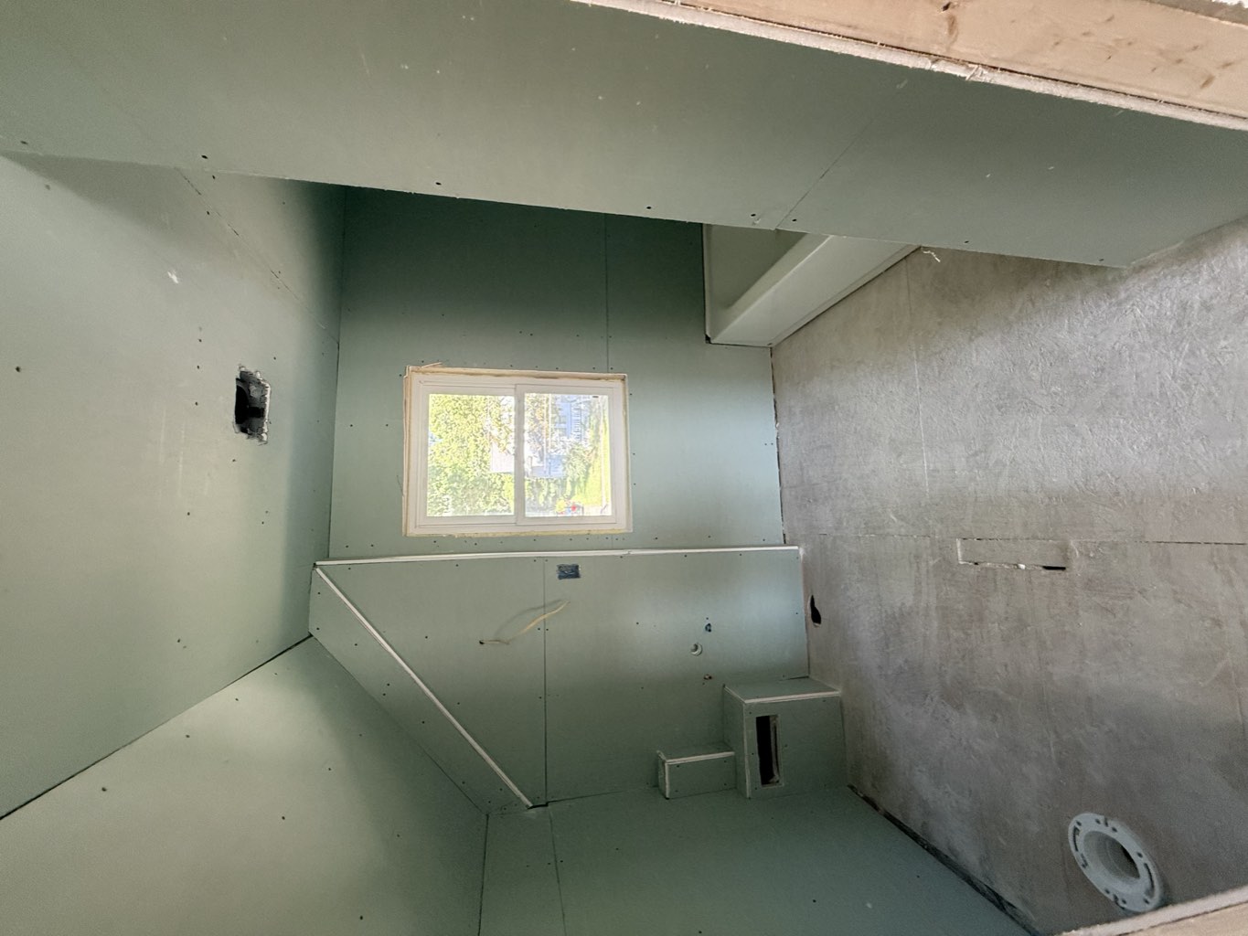 Upstairs bathroom under the sloped ceiling with green board and a new tub by the window.