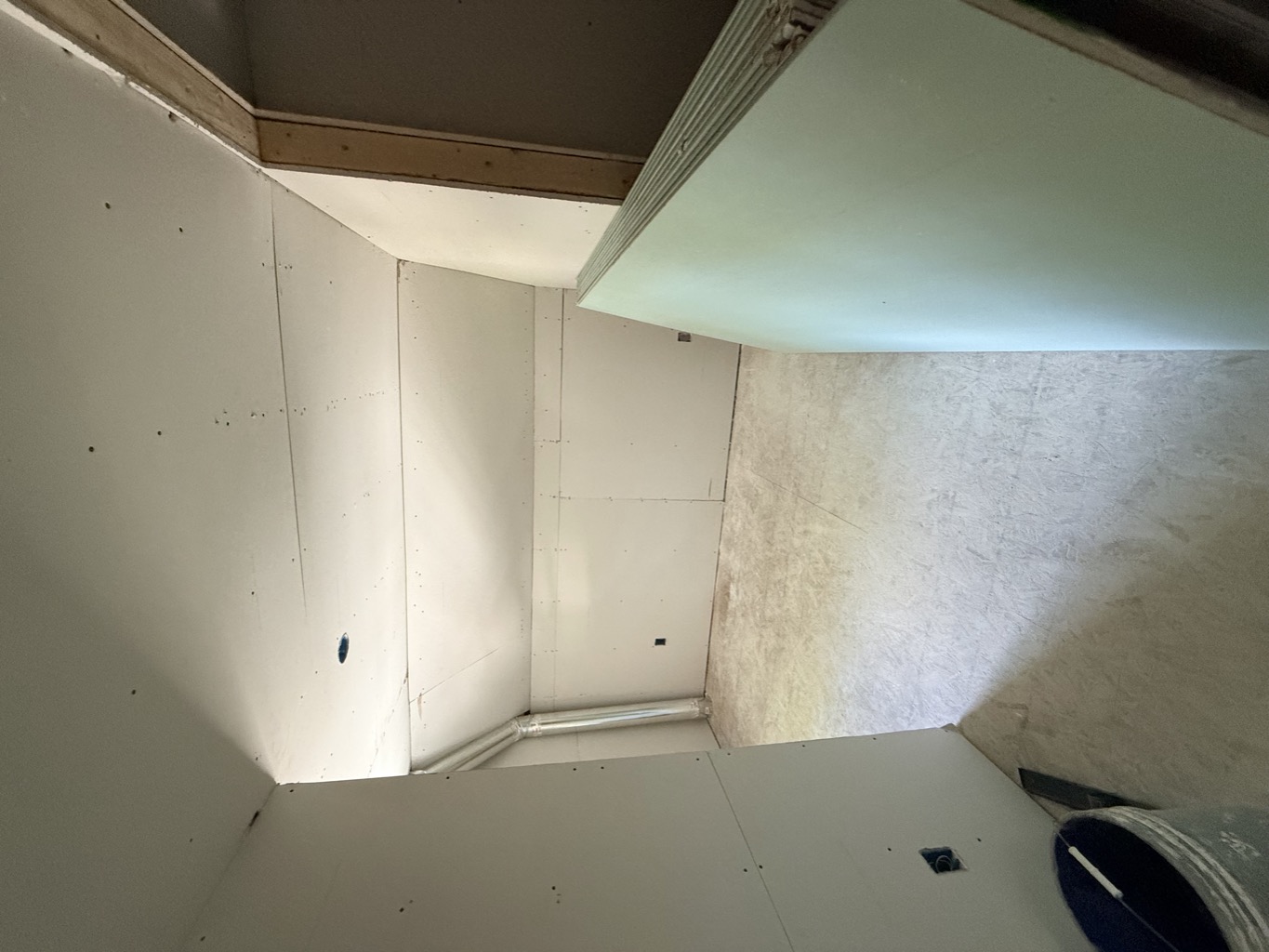 Upstairs room under the roofline hung with drywall, sheets of green board leaning at the side.